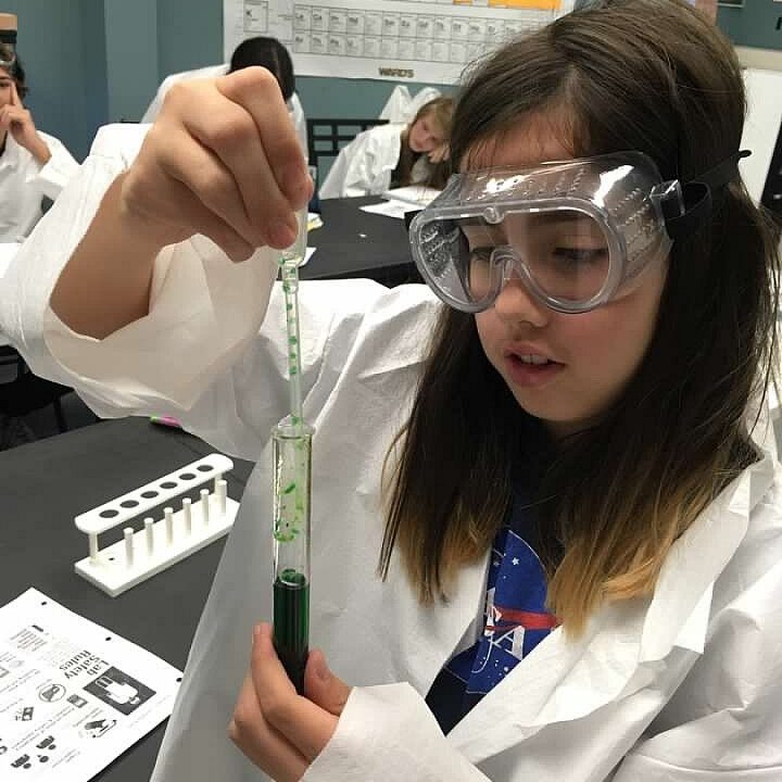 girl with science goggles fills a test tube